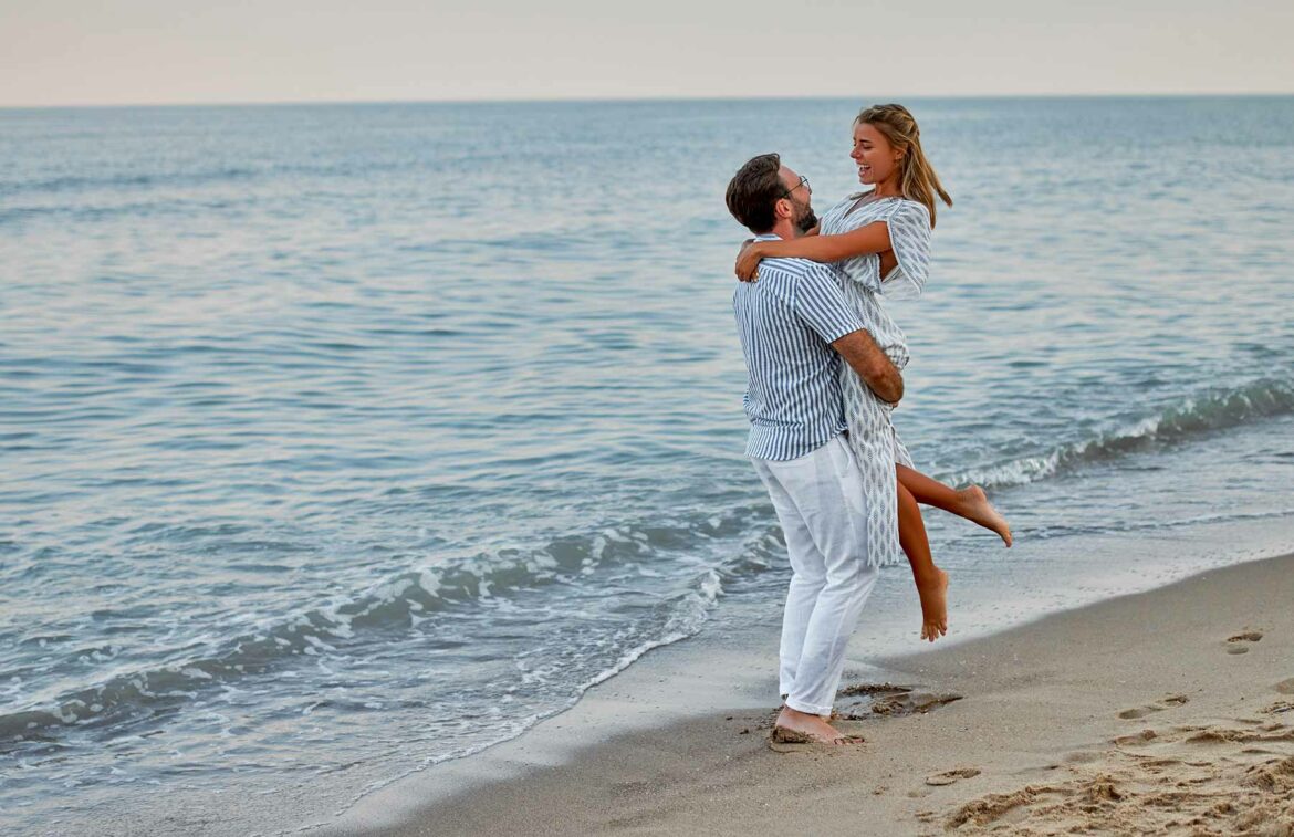 Engagement Ring Alternative: A couple on a vacation embracing on a beach with waves in the background