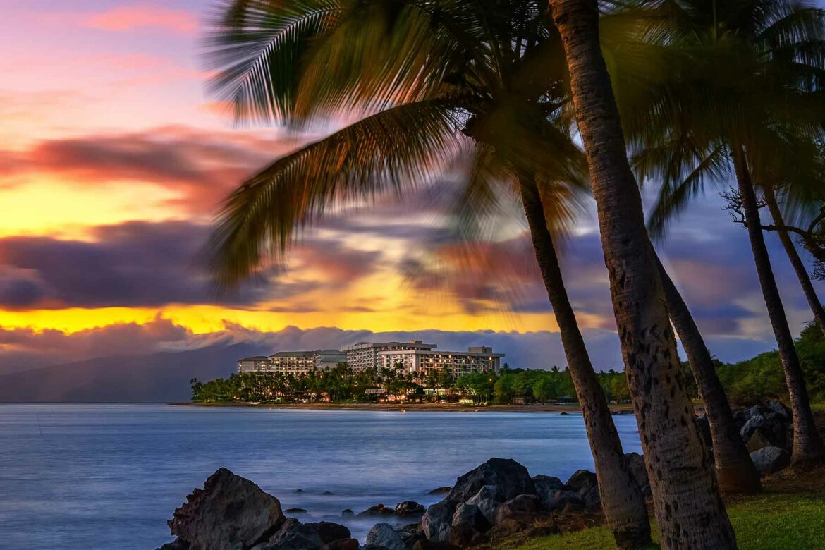 Hawaii honeymoon resort in the distance surrounded by water and palm trees at sunset