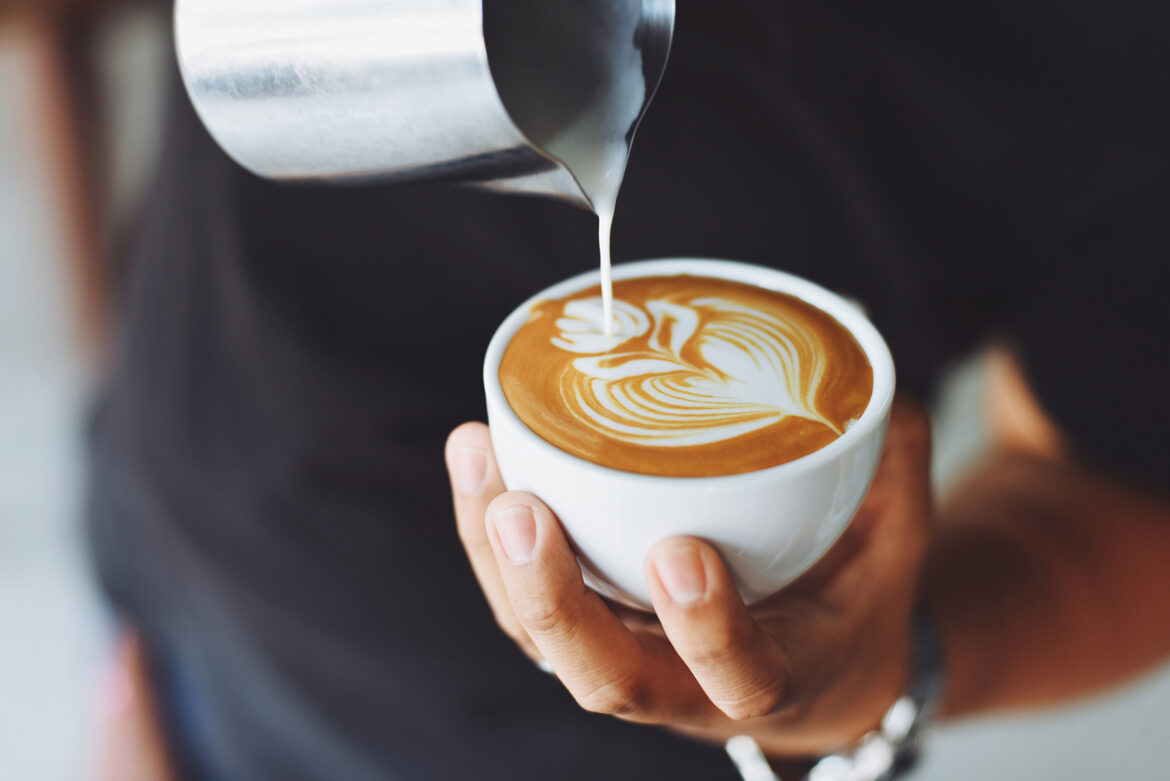 Frothed milk being poured into a white coffee cup to create a design