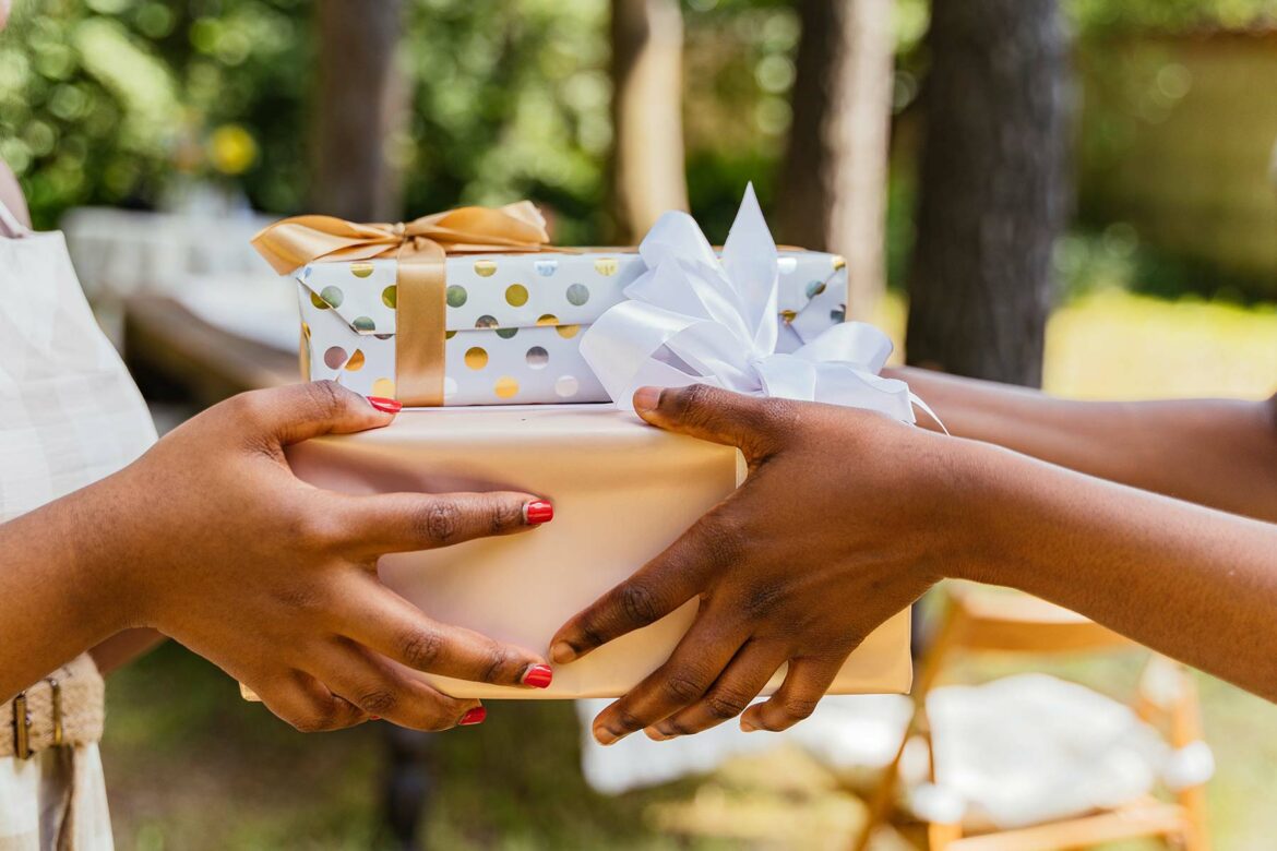 Two outstretched hands holding wedding shower gifts wrapped in shiny paper with bows