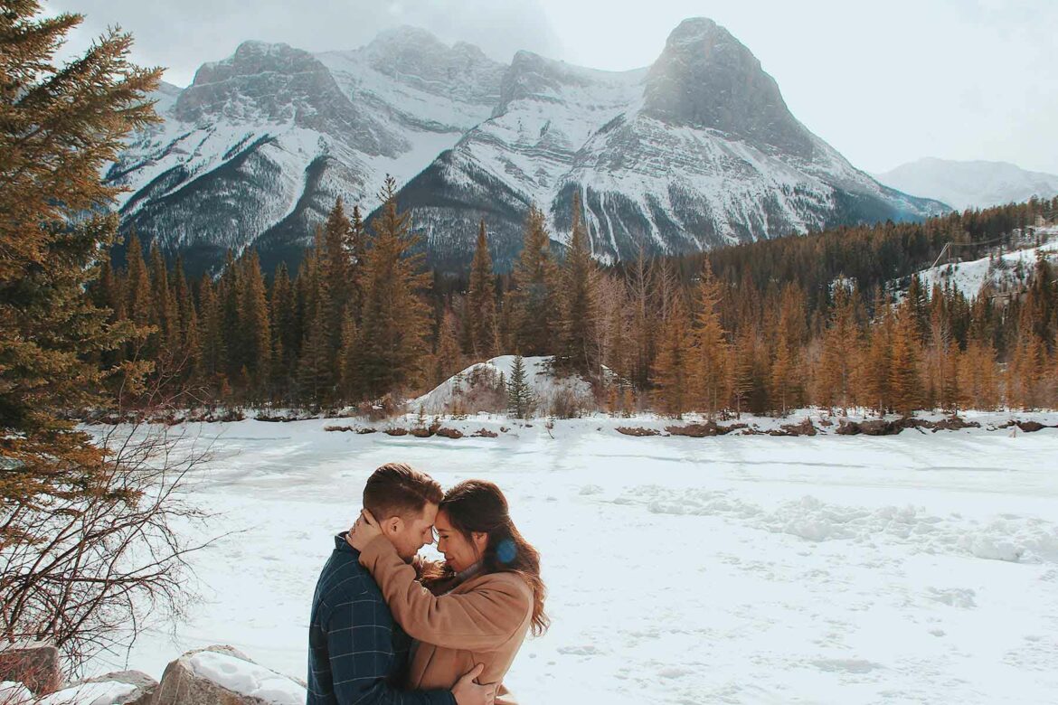 A couple putting their heads together in front of snow-covered mountains