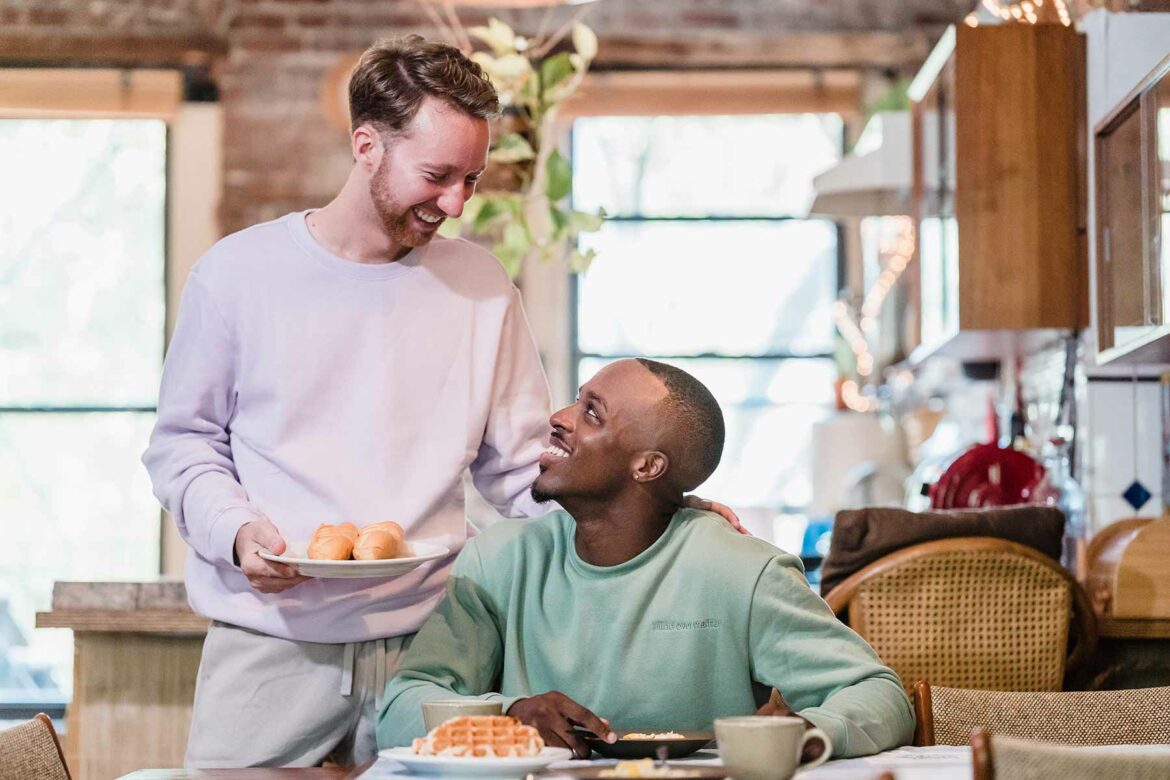 Man presents a plate of pastries to his spouse at the kitchen table