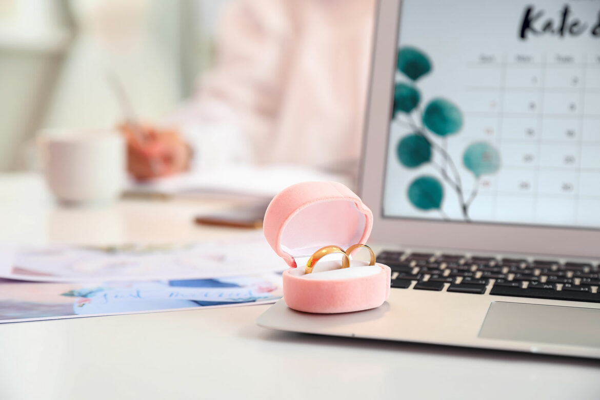 An ring box holding two gold wedding rings sits on the edge of an open laptop with a countdown calendar