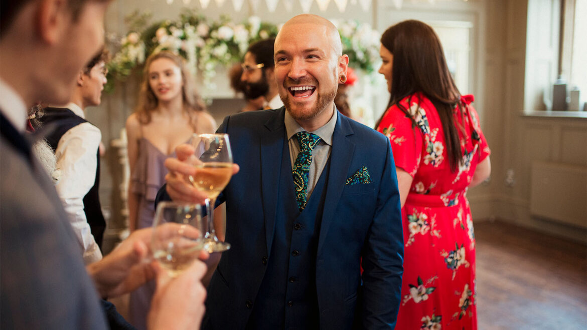 Wedding guest in semi-formal suite and tie toasts a wine glass with fellow guests